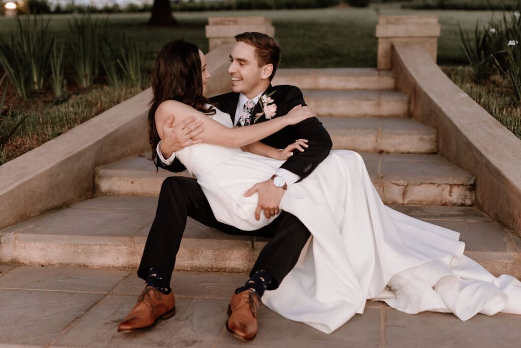Bride sitting in grooms lap on outdoor concrete staircase