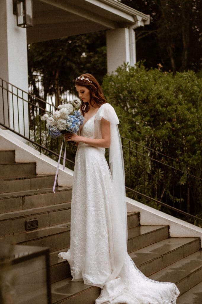 Bride standing on outdoor concrete staircase looking down at bouquet