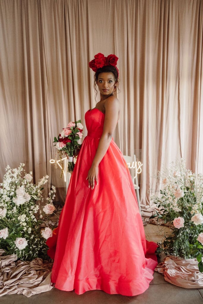 Fashion show model wearing red wedding dress with red crown headband standing sideways
