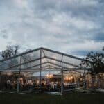 Clear marquee set up with tables and lights in the evening