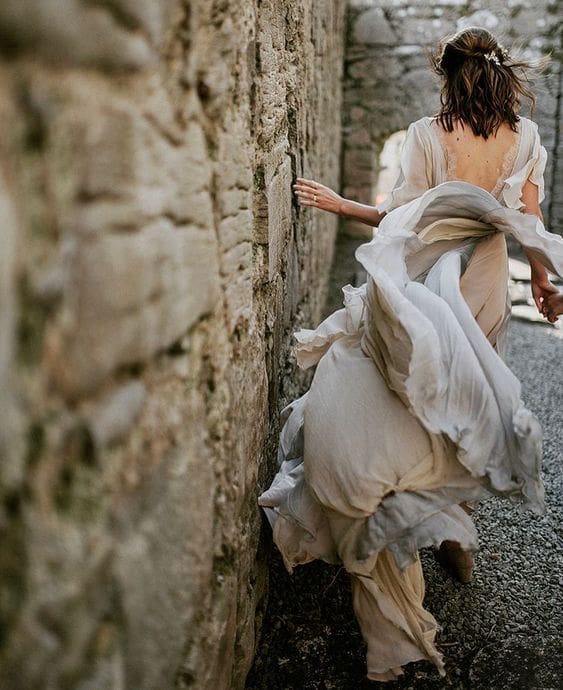Bride walking along wall with whipping dress behind