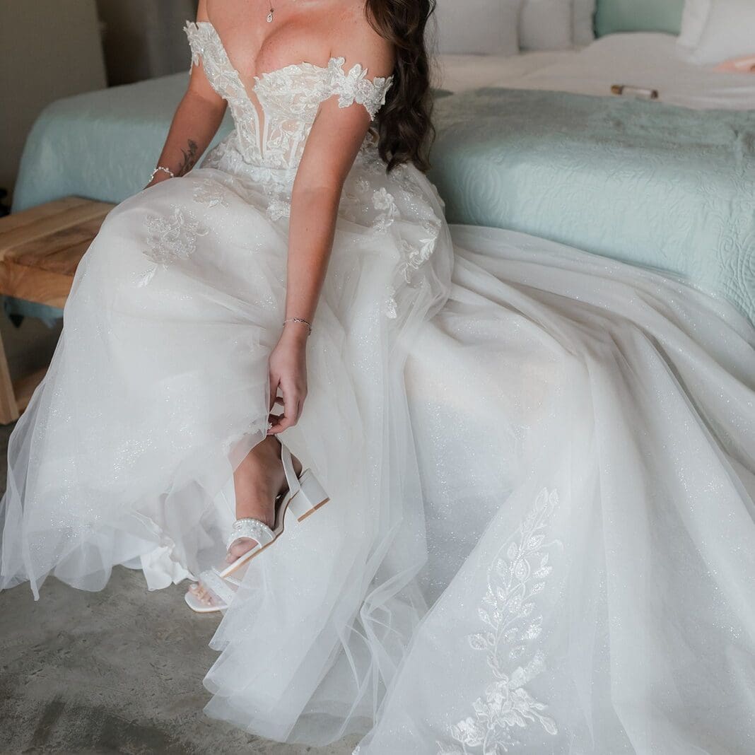 Bride sitting on the edge of a bed putting her heels on